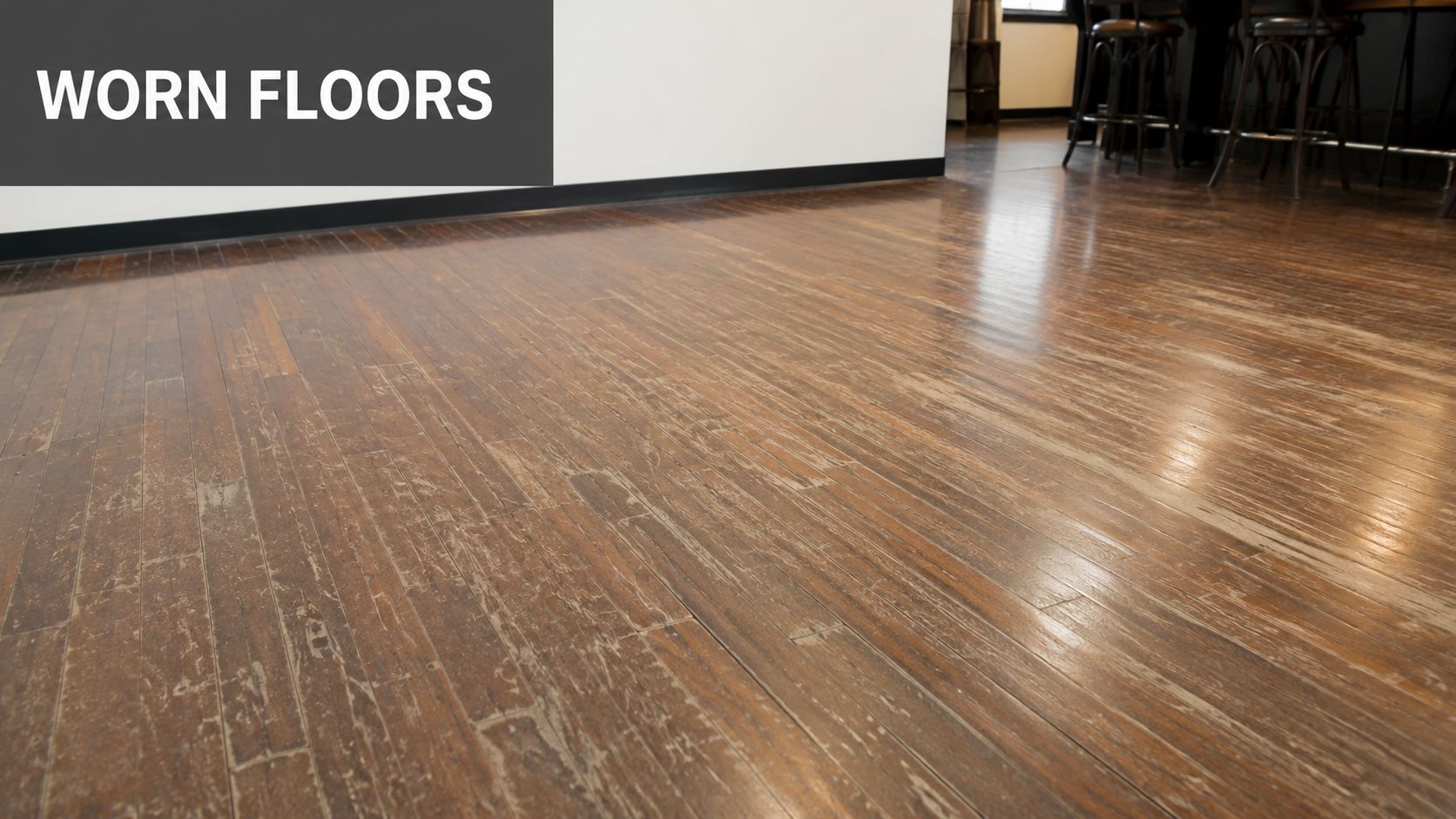A perspective view of a worn and distressed commercial hardwood floor with visible surface scratches and wear.
